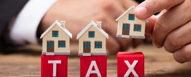 Businessperson placing house model over tax word blocks