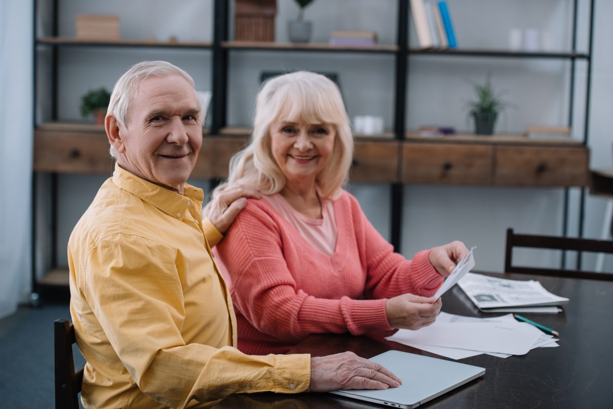 A senior couple smiling and sitting at desk with papers.