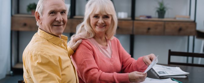 A senior couple smiling and sitting at desk with papers.